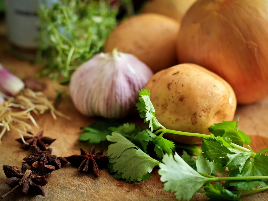 Kartoffeln, Knoblauch und frische Kraeuter auf einem Holzbrett